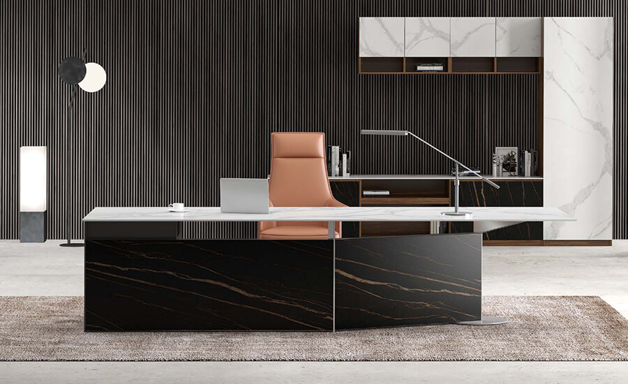 Г-образный стол из черного и белого спеченного камня с оранжевым стулом с высокой спинкой за книжным шкафом из спеченного камня.